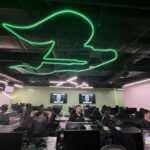 A row of computers with students playing video games, and above them, a large neon USF logo