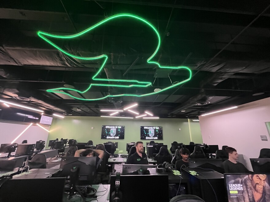 A row of computers with students playing video games, and above them, a large neon USF logo